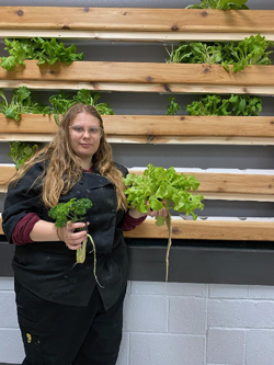 student holding plants with wall of plants in the background